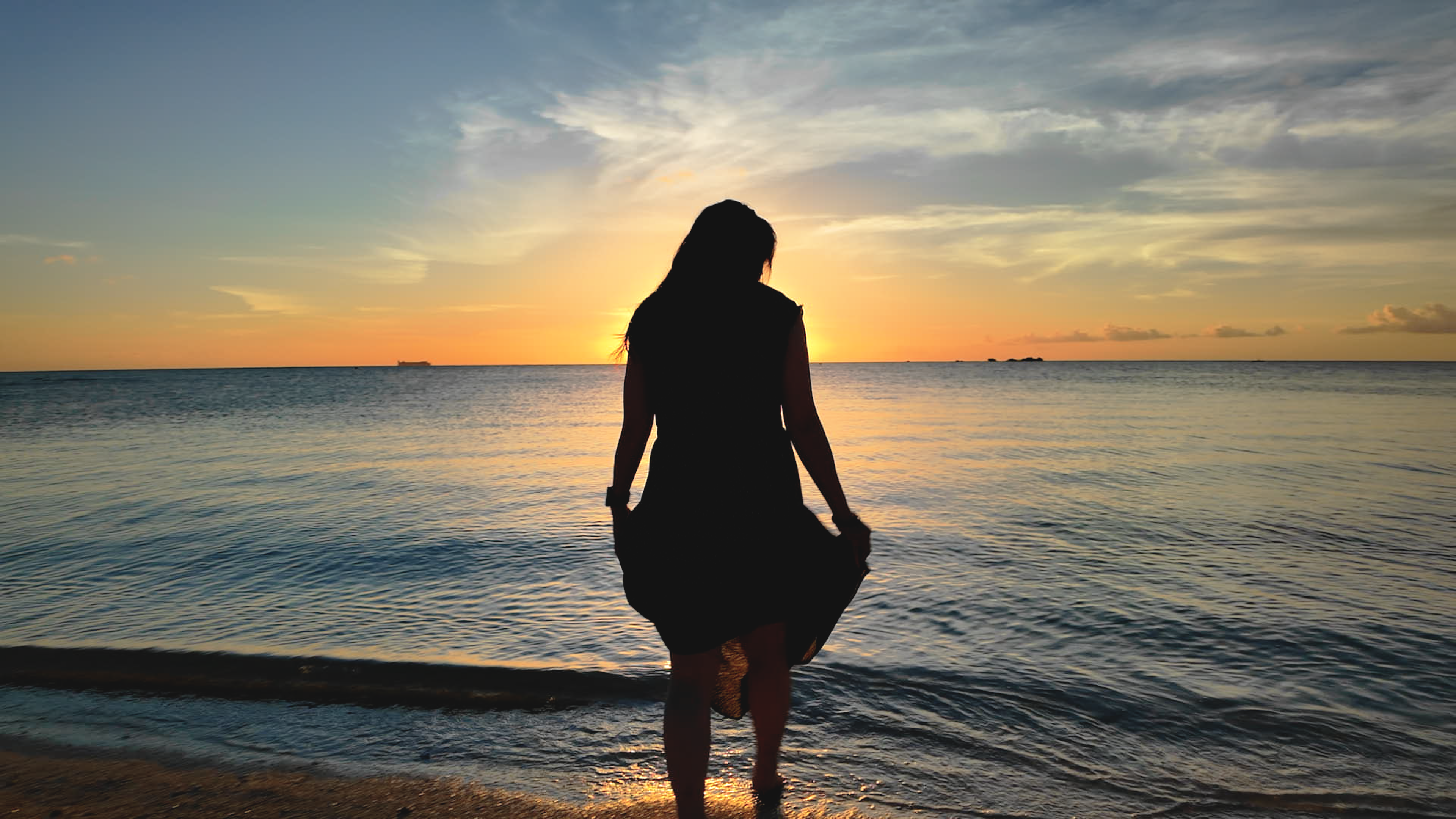 夕暮れのビーチに立つ女性のシルエット